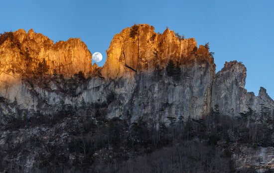 The setting sun light touches the face of Seneca Rocks as the moon rises through the notch, wide angle photo taken in West Virginia by David S. Johnston.